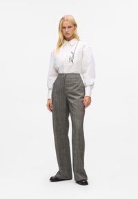 White button-up shirt with puffed sleeves and black embroidered detail, paired with high-waisted gray plaid trousers and black shoes.