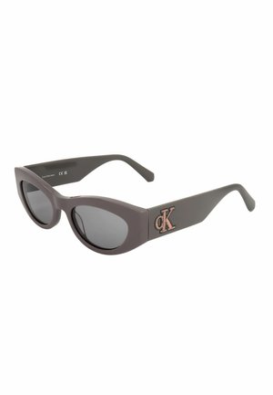 Occhiali da sole neri a forma di cat-eye con lenti scure e logo Calvin Klein "cK" rosa sulla asta.