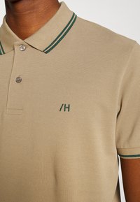 Polo beige con tessuto testurizzato, colletto a righe verdi, due bottoni e logo ricamato sul petto.