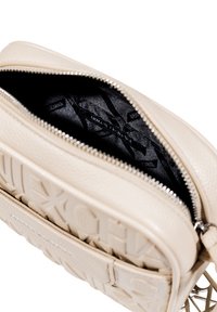 Borsa in pelle beige testurizzata con logo in rilievo, dotata di una cerniera argentata e di un interno in tessuto nero con etichetta del marchio.