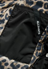 Tissu en imprimé léopard noir et beige avec une texture lisse ; comprend une poche noire avec une étiquette tissée portant le texte "ALLSAINTS."