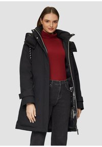 Zwarte geïsoleerde jas met een capuchon, rits- en drukknoopsluitingen, en zijzakken; gedragen over een rode coltruien en donkere jeans. Gladde textuur.