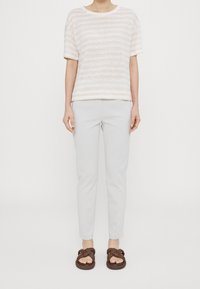 Camiseta rayada color beige claro, de corte holgado, con mangas cortas; combinada con pantalones gris ajustados; sandalias trenzadas marrones. Diseño simple y texturizado.