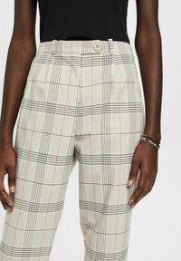 Gecontroleerde broek in lichtbeige, met een zwart en rood vierkant patroon, hoge taille, plooien en een knoopsluiting bij de taille.