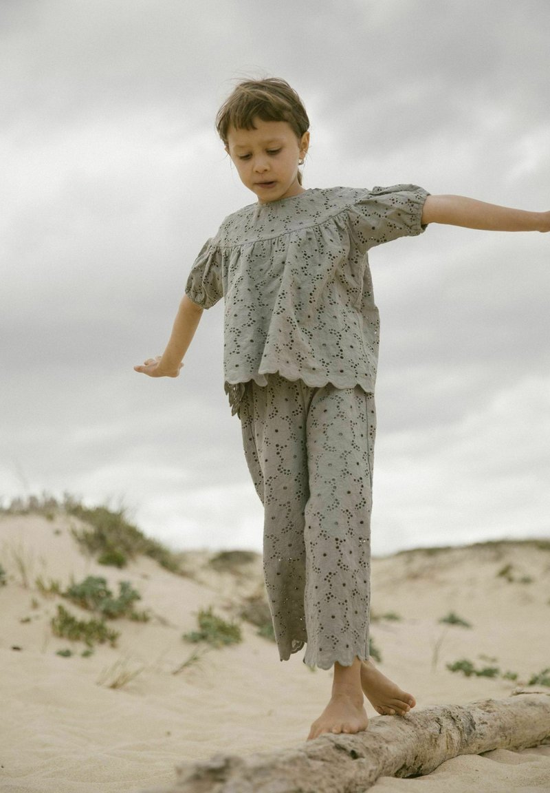 Completo in cotone grigio composto da una blusa con maniche a sbuffo e dettagli ricamati, abbinata a pantaloni coordinati. Il tessuto ha una consistenza delicata.