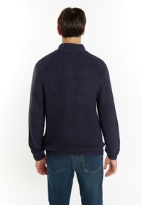 Maglione lavorato a maglia blu navy con colletto alto, texture a coste e maniche lunghe; abbinato a jeans in denim blu.