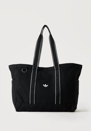 Sort canvas-tote taske med to lange håndtag, hvid syning, sidelommer, metalring og lille hvid Adidas-logo foran.
