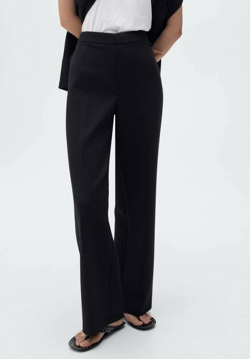 Pantaloni neri a vita alta con un design a gamba dritta, caratterizzati da una texture liscia e linee pulite. Abbinati a una blusa bianca e sandali.