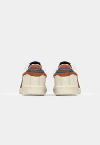 White leather sneakers featuring brown suede accents, blue detailing at the heel, and textured rubber soles. Classic low-top design.