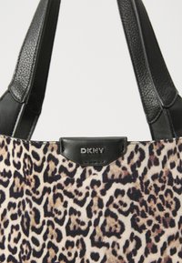 Leopárdmintás vászontáska puha textil külsővel, fekete bőr kiegészítőkkel és DKNY logóval egy letisztult fekete folton. Két fekete fogantyú.