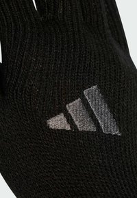 Černé pletené rukavice s texturovaným designem a reflexním stříbrným logem adidas. Materiál vypadá měkký a pružný.