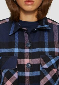 Flanellen overhemd in marineblauw, roze en lichtblauw ruitpatroon. Voorzien van een kraag, twee borstzakken en zwarte knopen. Getextureerde stof.