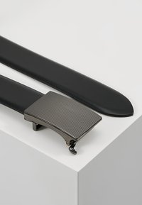 Ceinture en cuir noir avec une boucle en métal rectangulaire présentant une texture striée et un mécanisme de clip pour le réglage. Bords et finition lisses.