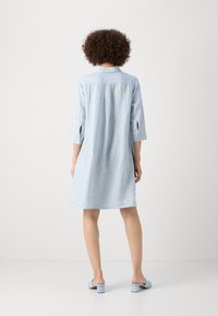 Lichtblauw gestreepte jurk met driekwart mouwen, afgeronde zoom en uitsparingen bij de mouwen. G gedragen met lichtblauwe hoge muil.