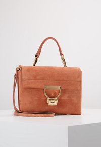 Prostokątna torebka z zamszu w kolorze przybrudzonego różu, z zapięciem w złotym odcieniu, górnym uchwytem i odczepianym paskiem na ramię, umieszczona na białej powierzchni.