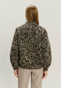 Sweter z nadrukiem w panterkę w odcieniach szarości i brązu, z wysokim kołnierzem, prążkowanymi mankietami i luźnym krojem. Noszony z jasnymi spodniami.