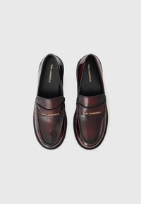 Błyszczące burgundowe skórzane loafersy z haftowanymi detalami i płaską podeszwą. Na pasku znajduje się złoty napis "KARL LAGERFELD".