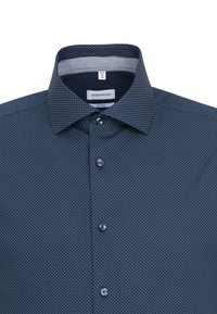 Granatowa koszula w białe kropki, z klasycznym kołnierzykiem, zapinana na guziki i o teksturowanym wykończeniu tkaniny. Widoczna metka marki.