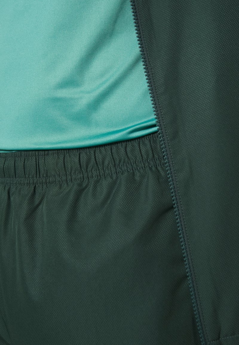 Conjunto deportivo de dos piezas que presenta una blusa de color azul claro hecha de tela suave y shorts de cintura elástica de color verde oscuro con un acabado texturizado.