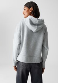 Felpa grigia con cappuccio, dal taglio rilassato, texture morbida e polsini a costine. Indossata con jeans di denim scuro, vista posteriore.