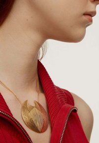 Collar de canalé rojo con un collar de oro que tiene un diseño abstracto ondulado, con finas líneas y un detalle recortado.