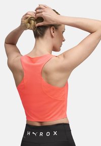 Bright orange athletic tank top with a textured fabric, a racerback design, and an asymmetrical hem. Paired with black high-waisted leggings.