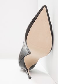 Svart lackläder stilettklack med spetsig tå, med en slät yta, nude inredning och en elegant silhuett.