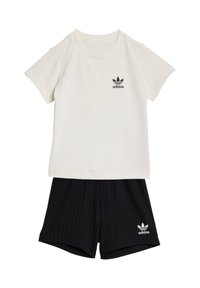Conjunto de camiseta blanca de manga corta acanalada de Adidas con pantalones cortos negros acanalados de Adidas, que presentan los logotipos de trébol de Adidas en ambas prendas.
