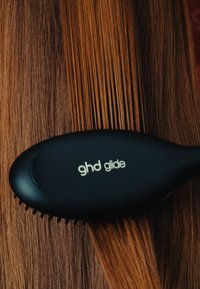 Szczotka do włosów GHD Glide z czarną ergonomiczną rączką, wyposażona w drobne włosie, sunąca po gładkich, prostych brązowych włosach.