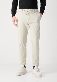 Beiga, lätta byxor med elastisk midja och snörning. Kombinerat med vita sneakers med mörka detaljer. Rak skärning.