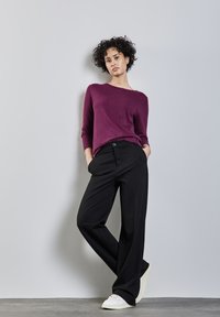 Lila langärmeliger Pullover kombiniert mit schwarzen weit geschnittenen Hosen und weißen Sneakers. Das Outfit hat einen lässigen Schnitt und dezente Texturen.