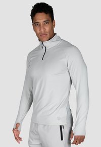 Graues langärmliges Sportoberteil mit einem Viertelreißverschluss-Kragen, aus einem glatten, dehnbaren Material, mit Daumenlöchern und dezentem Branding an der Seite.