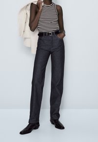 Black and white striped tank top, high-waisted dark blue denim jeans, black belt, and black ankle boots. Simple, fitted design with neutral colors.