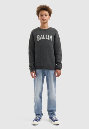 Grijze gebreide trui met "BALLIN" in witte letters, gecombineerd met lichtblauwe jeans en blauwe sneakers. Natuurlijke vezelstructuur zichtbaar.