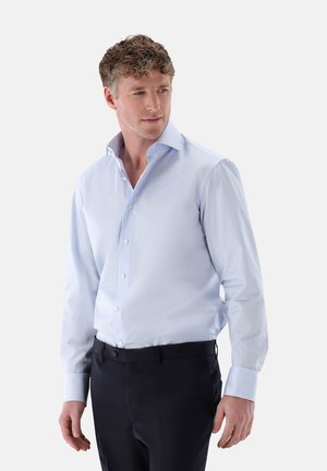 Hellblau gestreiftes Hemd mit spitzem Kragen; ausgestattet mit weißen Knöpfen, langen Ärmeln und einem schlanken Schnitt. Getragen mit dunklen Hosen.