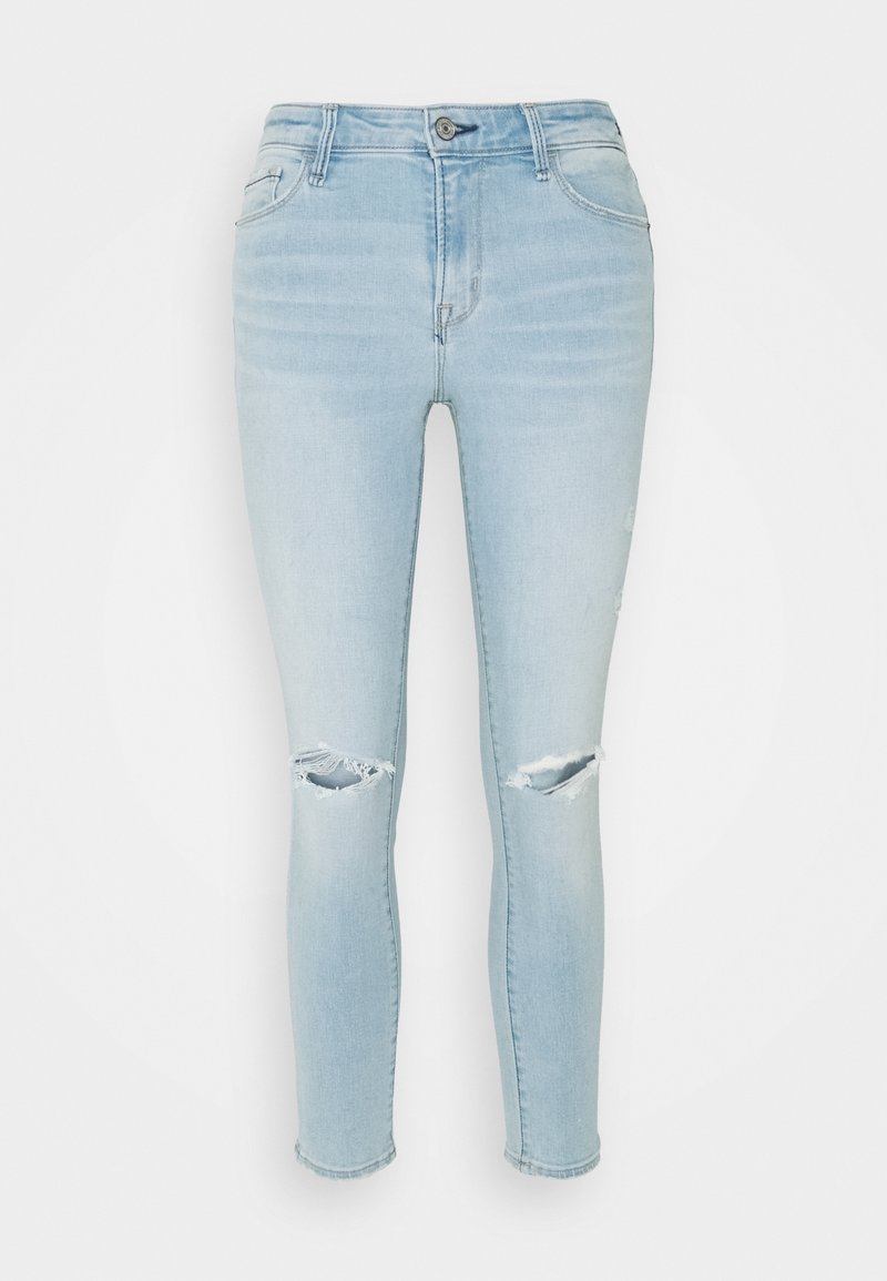 Jeans ajustados de mezclilla azul claro que presentan dos agujeros desgastados en las rodillas, cinco bolsillos y una cinturilla estándar con un cierre de botón en la parte delantera.