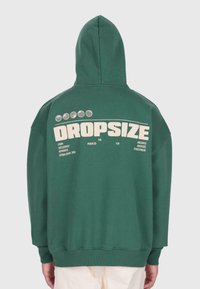 Haut à capuche vert avec la capuche relevée, présentant un grand texte blanc "DROPSIZE" ainsi que des textes plus petits et des graphiques circulaires au dos.