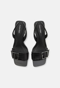 Black leather sandals with a square toe, thin straps, and a wide adjustable buckle detail. Smooth texture and minimalist design.