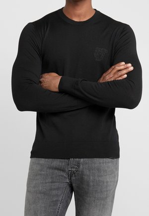 Pull noir à manches longues en coton, avec un col rond et des poignets côtelés, arborant un logo en relief subtil sur la poitrine gauche.