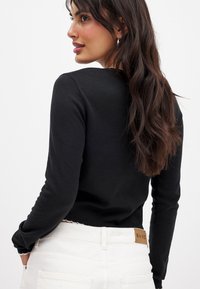 Zwarte fitted trui met een ronde halslijn, geribde manchetten en een licht rafelrandje, gecombineerd met witte high-waisted jeans.