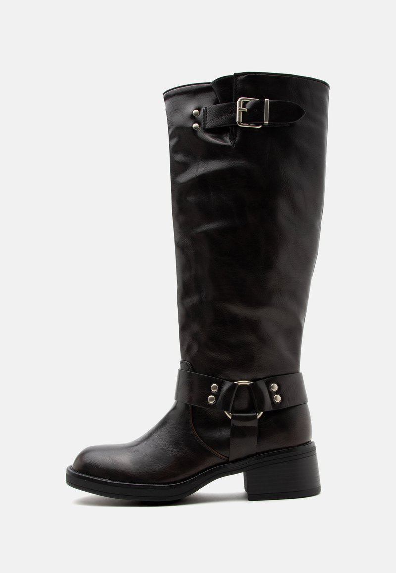 Botte en cuir noire montée jusqu’au genou avec un petit talon, bride décorative à boucle en haut et détail en forme d’anneau près de la cheville, vue de profil sur fond blanc.