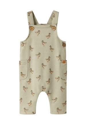 Salopette beige pour bébé avec des boutons en bois marron, deux poches latérales et un motif répétitif de canards imprimés sur tout le tissu.