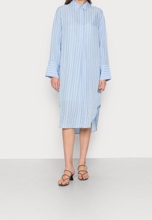 Hellblau gestreiftes Hemdkleid mit Kragen, langen Ärmeln und seitlichen Schlitzen, kombiniert mit braunen Riemchensandalen. Glatte Stoffstruktur.