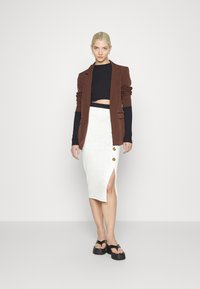 Blazer castanho, top cropped preto, saia midi branca com fenda lateral e acabamentos em botão, e sandálias de plataforma pretas. Design limpo e moderno.