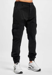 Zwarte cargobroek met elastische manchetten, meerdere zijzakken en een relaxte pasvorm, gemaakt van duurzame stof, gecombineerd met witte sneakers.