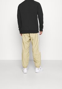 Svart sweatshirt med ribbade muddar och nederkant, ihop med beiga joggers med vita sidostråk, bärs med vita sneakers.