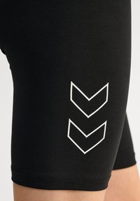 Czarne sportowe szorty o gładkiej fakturze i białym wzorze w chevron po bokach. Projekt ma dopasowany krój i długość do połowy ud.