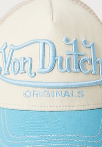 Beige and light blue baseball cap with embroidered "Von Dutch" logo and "ORIGINALS." Features curved brim and textured fabric.