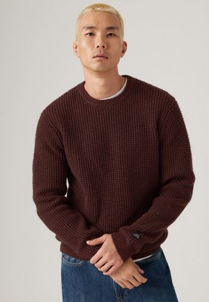 Burgundy knit sweater with textured pattern, crew neck, ribbed cuffs, and hem. Paired with blue denim jeans.