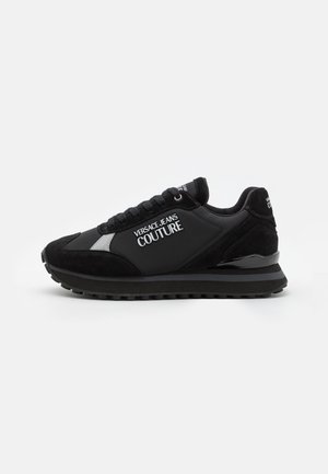 Sneaker nero Versace Jeans Couture con chiusura frontale con lacci, logo bianco sul lato, colletto imbottito e suola in gomma testurizzata su sfondo bianco.